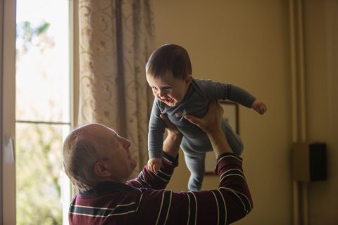 man wearing maroon, white, and blue stripe long-sleeved shirt lifting up baby wearing gray onesie